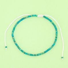 a blue beaded bracelet with white string and beads on it, against a green background