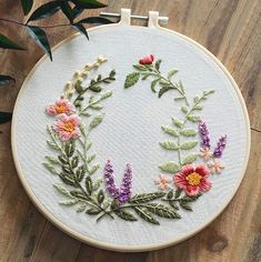 an embroidered wreath with flowers and leaves on a wooden surface