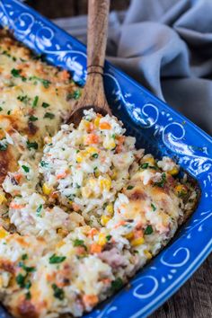 a casserole dish with rice and vegetables in it on a blue plate next to a wooden spoon