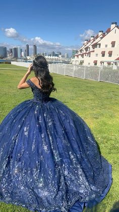 a woman in a blue ball gown sitting on the grass with her back to the camera