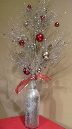 a christmas tree in a glass bottle on a table with red and silver ornaments around it