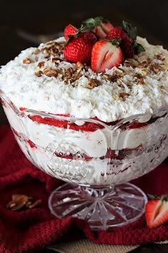 a dessert dish with strawberries and whipped cream in it on a red napkin next to a glass bowl