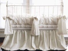 a white crib with ruffled bedding in front of a window and wooden floor