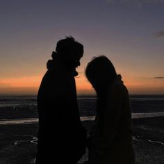 two people standing next to each other in front of the ocean at sunset or dawn