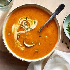 there is a bowl of soup on the table with two bowls and spoons next to it