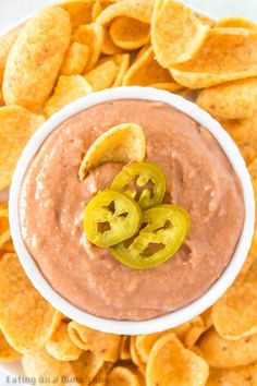 a white bowl filled with chips and a red dip surrounded by sliced jalapenos