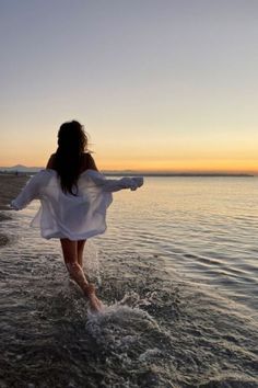 a woman walking into the ocean at sunset