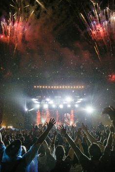 fireworks are lit up in the night sky above a crowd at an outdoor music festival