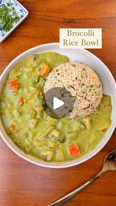 a bowl filled with rice and vegetables on top of a wooden table next to a spoon