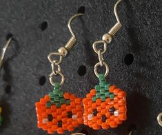 two orange and green beaded pumpkins are hanging from silver hooks on a black surface