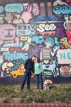 a man and woman standing next to each other in front of a wall covered with stickers