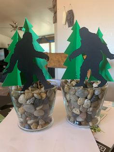 two paper cut out trees sitting on top of rocks in a glass vase filled with pebbles