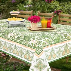 an outdoor table with fruit and drinks on it in front of some flowers, grass