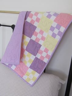 a bed with a purple and yellow quilt on it's headboard next to a white wall