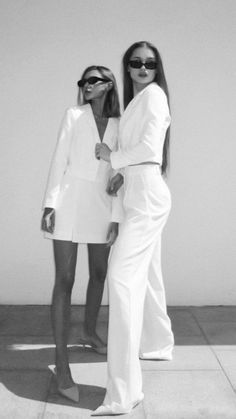 two women standing next to each other in white outfits and sunglasses, both wearing sun glasses