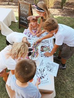 a group of children standing around a table with pictures on it and writing on the paper