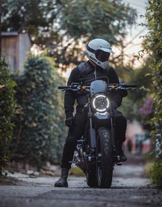 a man riding on the back of a motorcycle down a dirt road next to trees