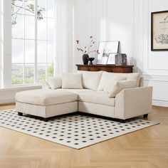 a white sectional couch sitting on top of a hard wood floor next to a window