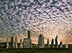 a group of rocks sitting on top of a lush green field under a cloudy sky