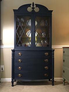 a blue china cabinet with glass doors and drawers in a room that has beige walls