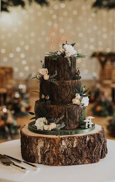 a three tiered wedding cake with flowers and greenery sits on top of a tree stump