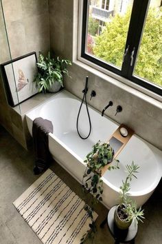 a bath tub sitting next to a window with plants on the floor and potted plants