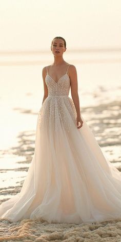 a woman standing on top of a beach next to the ocean wearing a wedding dress