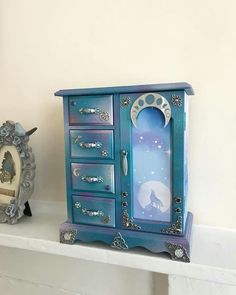 a blue cabinet sitting on top of a white shelf next to a clock and an owl figurine