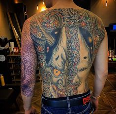 the back of a man with tattoos on his upper and lower half, wearing blue jeans