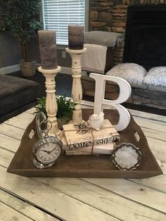 a wooden tray topped with candles and books on top of a coffee table next to a clock