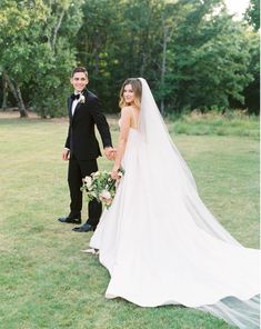 a bride and groom standing in the grass holding each other's hands with trees in the background