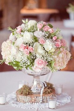 a vase filled with pink and white flowers on top of a table next to candles