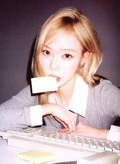 a woman sitting in front of a computer keyboard and holding a piece of paper to her mouth