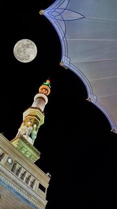 an illuminated clock tower with the moon in the sky above it and a blue canopy over it