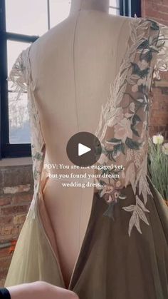 the back of a dress on display in front of a brick wall with flowers and leaves