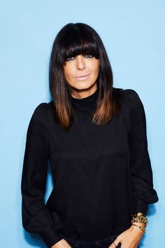 a woman with long hair wearing a black sweater and bracelets standing in front of a blue background