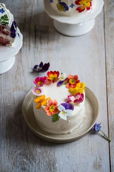 a white cake with flowers on it sitting on top of a wooden table next to two plates