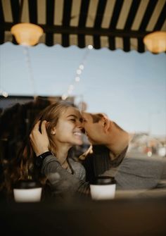 a man and woman are kissing in front of a window with coffee cups on the table