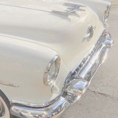 the front end of an old white car with chrome trim and hood ornaments on it