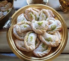 several pastries in a gold bowl on a wooden table next to cups and saucers