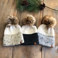 three knit hats with pom - poms sitting on top of a wooden floor