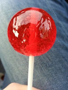 a close up of a person holding a red lollipop on a stick in their hand