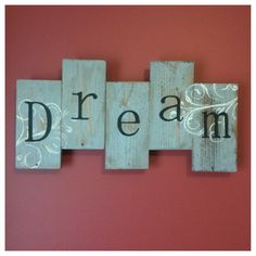 three wooden blocks with the word dream written on them in black and white ink against a pink wall