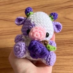 a small crocheted stuffed animal is held in someone's hand on a wooden surface