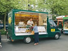 a man and woman standing in front of a green food truck with an open door