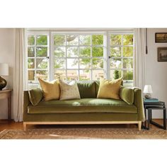 a green couch sitting in front of a window next to a table with a lamp on it