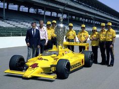 a group of men standing next to a race car with a trophy on the back