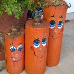 three wooden logs with faces painted on them sitting next to a potted planter