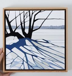 a person holding up a painting in front of a white wall with trees on it