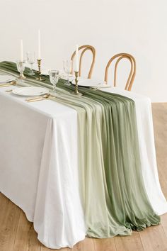 the table is set with white and green linens, gold place settings and candles